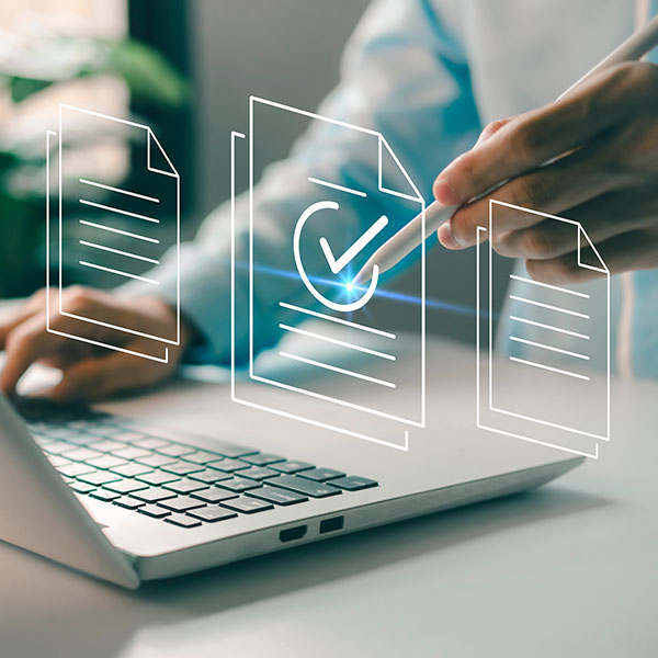 A person uses a stylus to interact with a laptop, surrounded by digital document icons. One document is highlighted with a checkmark, symbolizing completion or approval. The image conveys concepts of digital workflow, document management, or electronic approvals. Photo credit: Shutterstock