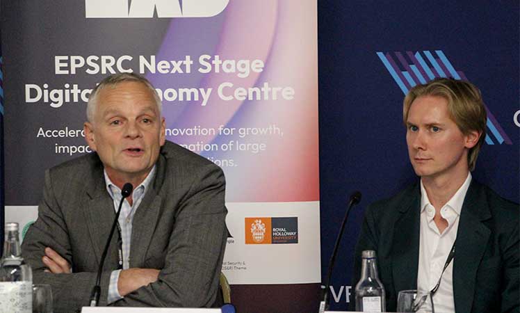 Prof. Mark Thompson speaks into a microphone while Dan Butler listens during a panel session.