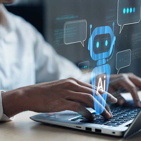 A close-up of a person typing on a laptop, with a glowing AI chatbot icon and speech bubbles hovering above the screen, representing the concept of artificial intelligence and virtual assistance. Photo credit: Shutterstock