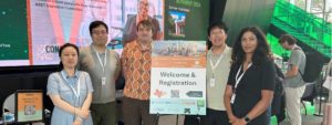 Group of five people posing indoors beside a “Welcome & Registration” sign; digital screen behind them shows info about Dr. Yvette E. Pearson and Summer 2025 Final Exam schedule